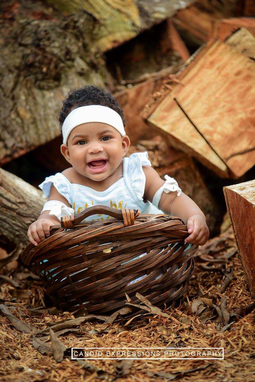 A smiling baby in a woven basket during an outdoor session